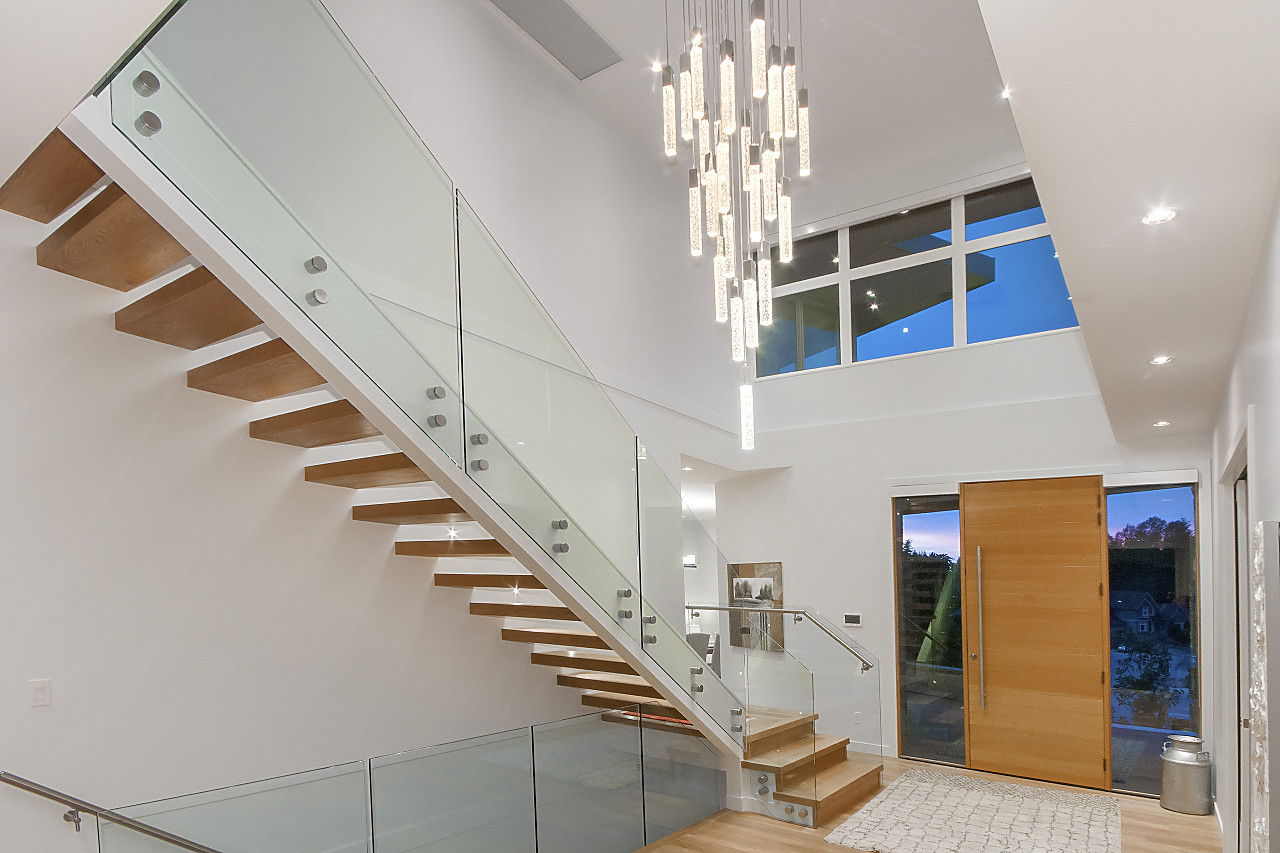 Two-storey foyer with floating wood staircase, glass railing, and crystal pendant chandelier