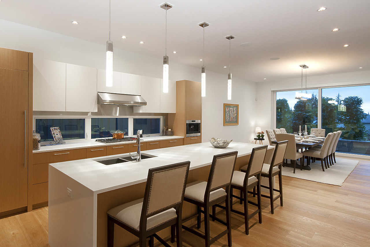 Open-plan kitchen with light wood cabinets, white quartz island, and crystal pendant lights