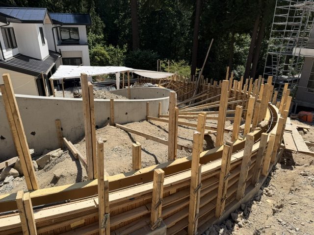 Stripped curved concrete wall and circular element beside modern West Vancouver homes