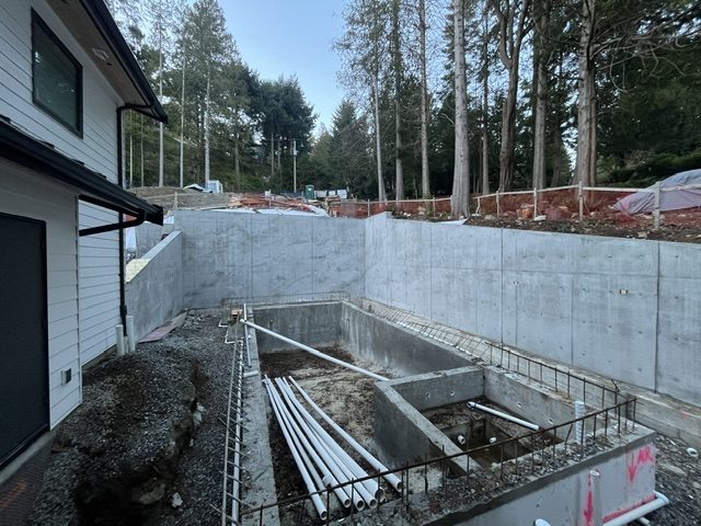 Finished cast-in-place structural retaining wall wrapping the backyard with the concrete pool shell in front, West Vancouver