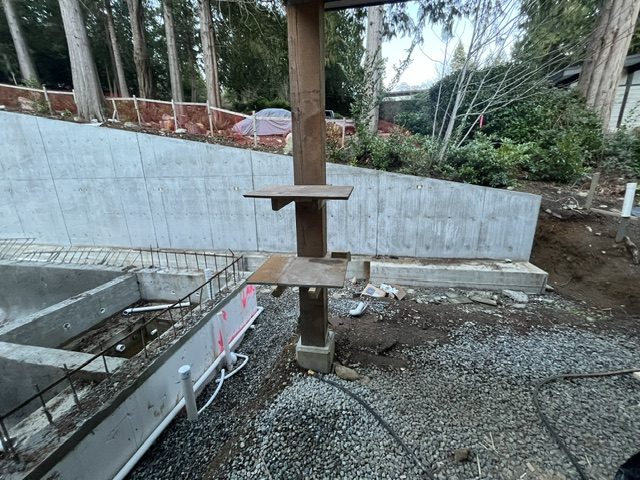 Board-formed structural retaining wall with a structural steel column on its footing beside the pool, West Vancouver