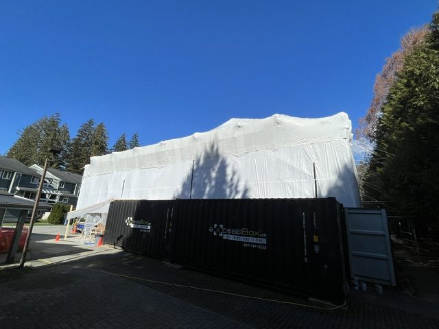 Multi-family building fully shrink-wrapped with on-site materials container during a roof upgrade
